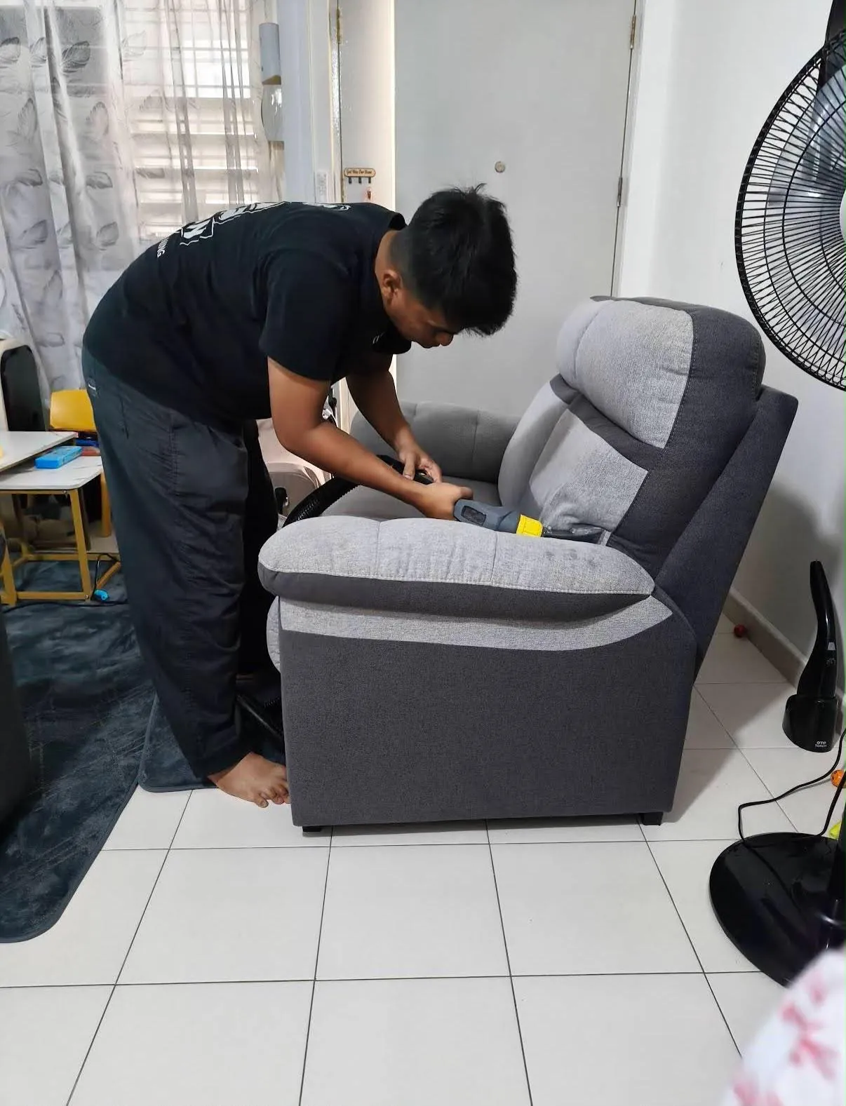 M Clean crew member cleaning a grey fabric recliner